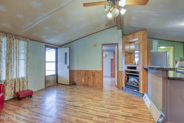 living area featuring a ceiling fan, wainscoting, lofted ceiling with beams, and light wood finished floors