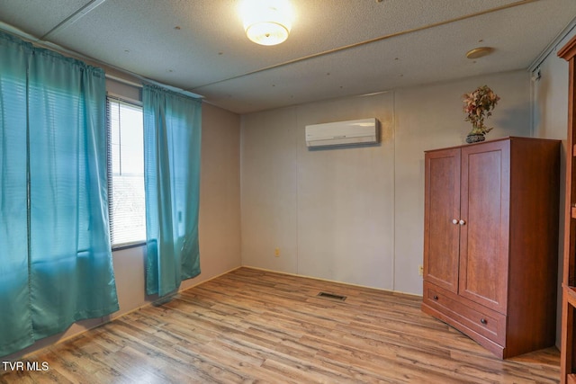 spare room with a wall unit AC, light wood-type flooring, visible vents, and a wealth of natural light