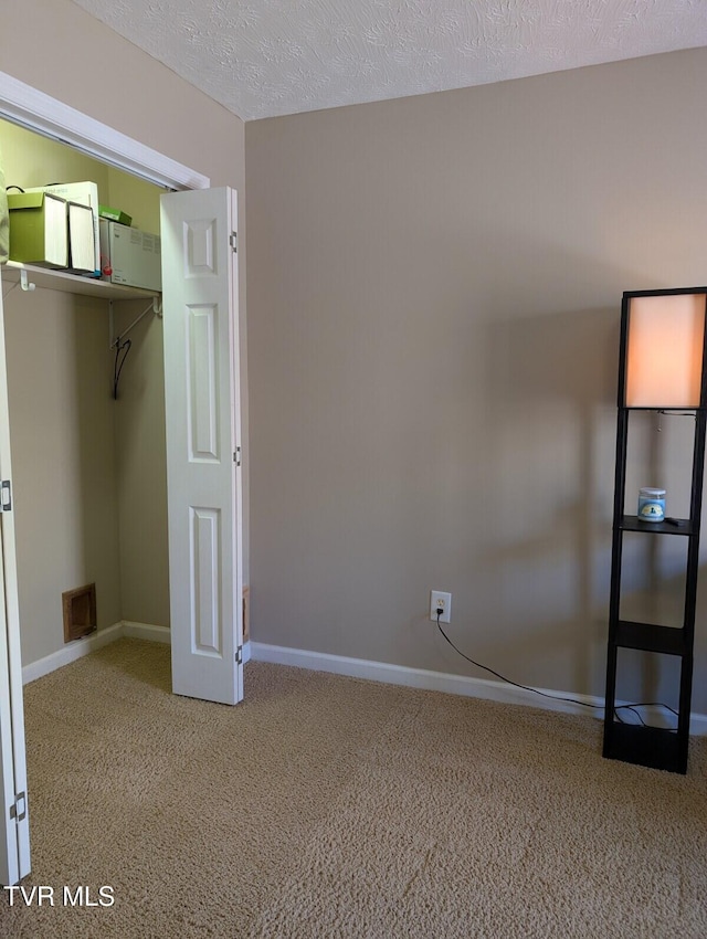 unfurnished bedroom featuring a textured ceiling, carpet, visible vents, and baseboards