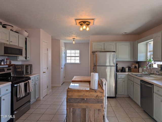 kitchen with stainless steel appliances, light tile patterned flooring, a sink, and light countertops