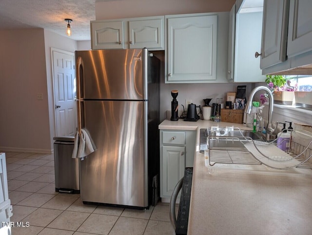 kitchen featuring light countertops, freestanding refrigerator, light tile patterned flooring, a sink, and a textured ceiling