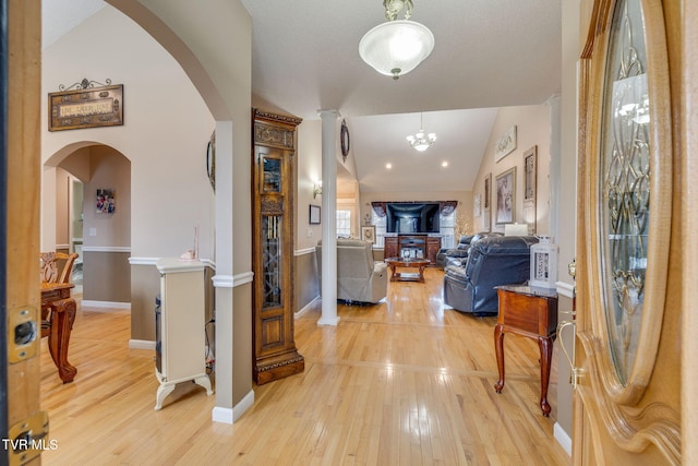 hallway with light wood-type flooring, baseboards, arched walkways, and vaulted ceiling