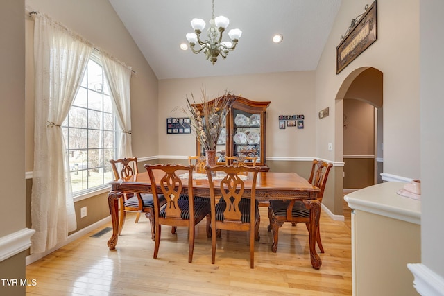 dining space with arched walkways, lofted ceiling, visible vents, light wood-style floors, and baseboards