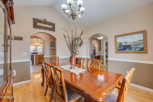 dining room featuring light wood-style floors, arched walkways, lofted ceiling, and an inviting chandelier