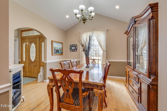 dining space featuring light wood finished floors, baseboards, arched walkways, and vaulted ceiling