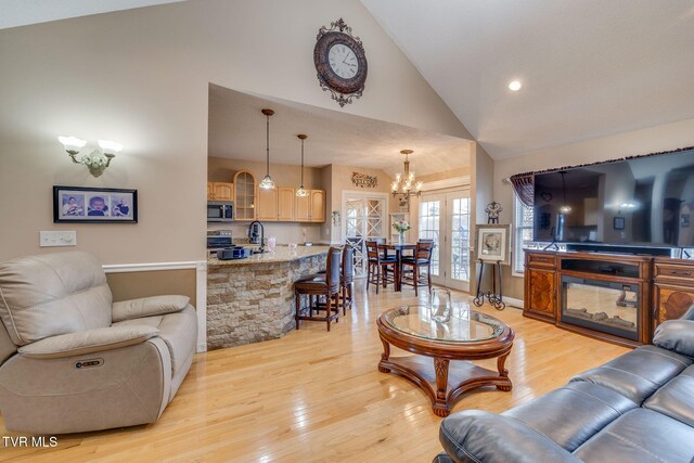 living room with high vaulted ceiling, a chandelier, french doors, and light wood finished floors