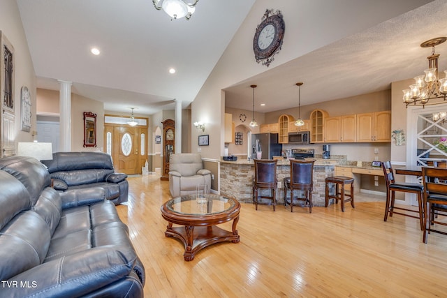 living room featuring a chandelier, high vaulted ceiling, light wood-style flooring, recessed lighting, and ornate columns