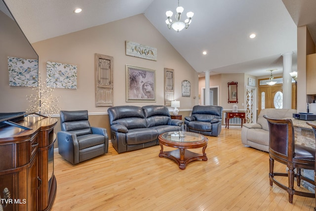 living area featuring high vaulted ceiling, light wood finished floors, an inviting chandelier, and ornate columns