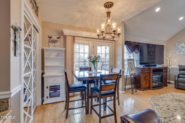 dining space featuring a textured ceiling, a chandelier, light wood-style flooring, baseboards, and vaulted ceiling