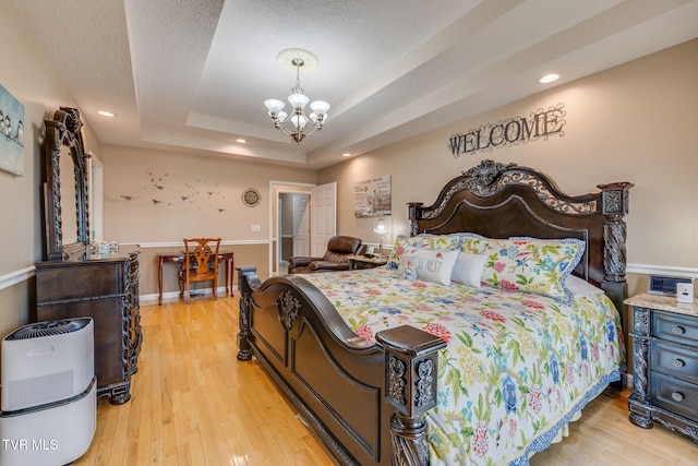 bedroom with a notable chandelier, a raised ceiling, a textured ceiling, light wood-type flooring, and baseboards