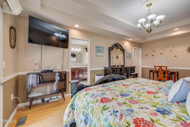 bedroom featuring a chandelier, wood finished floors, visible vents, baseboards, and a tray ceiling