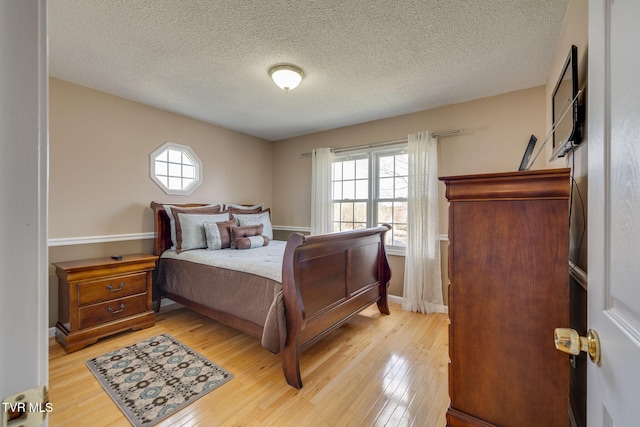 bedroom with light wood-style floors, a textured ceiling, and baseboards