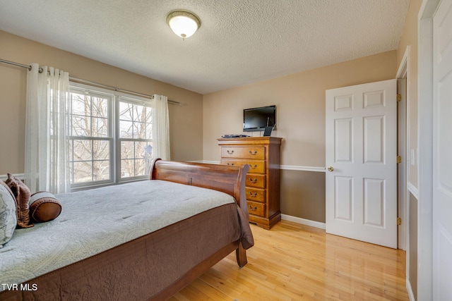 bedroom featuring light wood-style flooring, baseboards, and a textured ceiling