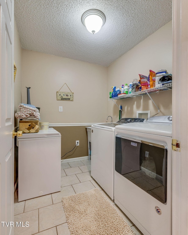 laundry area featuring laundry area, washer and clothes dryer, a textured ceiling, and light tile patterned flooring