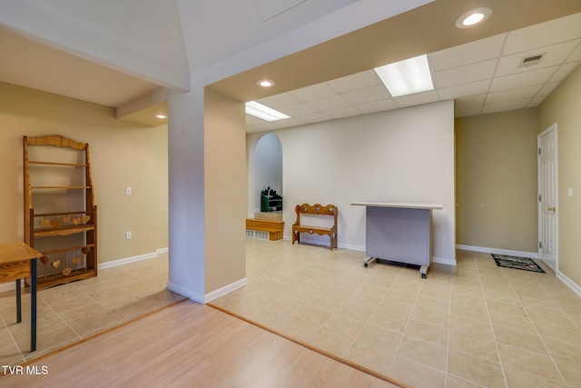 basement featuring arched walkways, a drop ceiling, visible vents, and baseboards