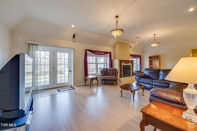 living room with lofted ceiling, light wood-style flooring, a fireplace with raised hearth, and recessed lighting