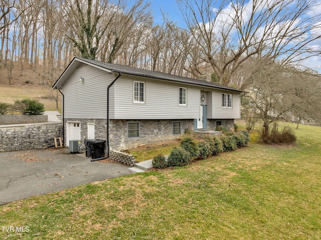 raised ranch featuring driveway, stone siding, a front yard, an attached garage, and central AC unit