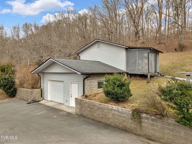 view of side of home featuring an attached garage, driveway, and roof with shingles