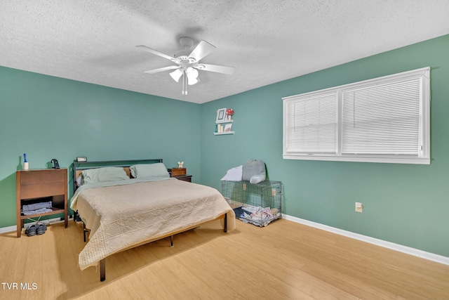 bedroom with ceiling fan, a textured ceiling, baseboards, and wood finished floors