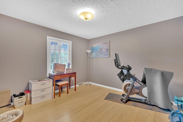 workout area with baseboards, a textured ceiling, and wood finished floors