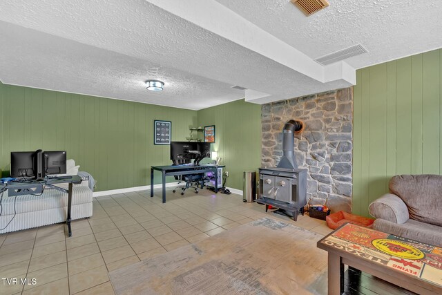 living area with tile patterned floors, visible vents, a textured ceiling, and a wood stove