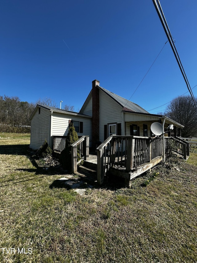 back of house featuring a chimney, a deck, and a lawn