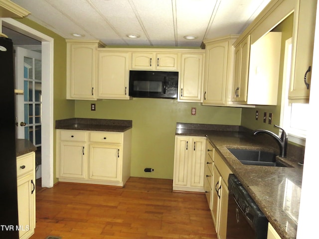 kitchen with dark stone counters, wood finished floors, cream cabinetry, black appliances, and a sink