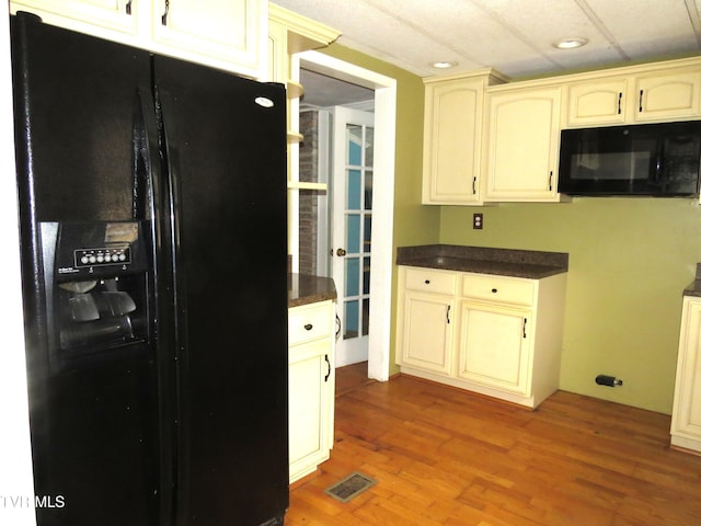 kitchen featuring dark countertops, visible vents, cream cabinets, wood finished floors, and black appliances