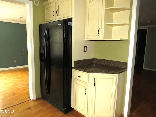 kitchen featuring light wood finished floors, black fridge with ice dispenser, and cream cabinetry