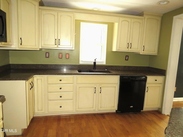 kitchen with cream cabinetry, dark countertops, dark wood-type flooring, a sink, and black appliances