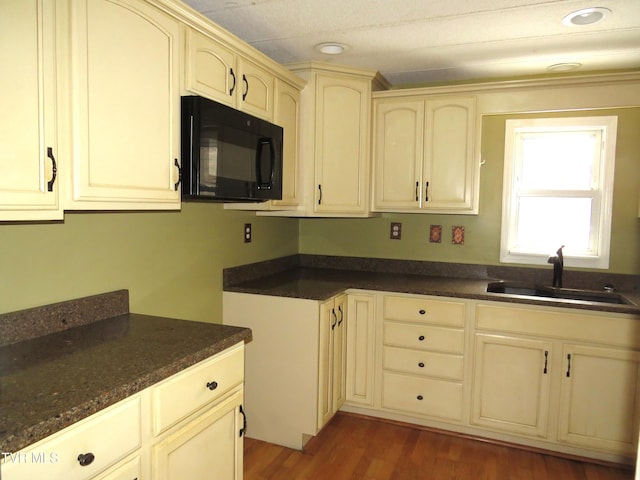 kitchen with black microwave, cream cabinetry, a sink, and wood finished floors