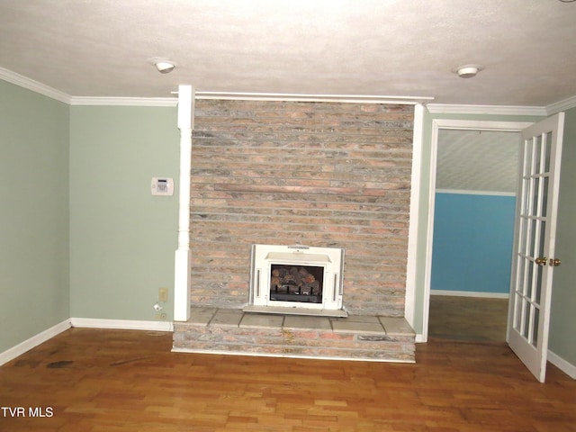 unfurnished living room featuring a fireplace with raised hearth, ornamental molding, wood finished floors, and baseboards