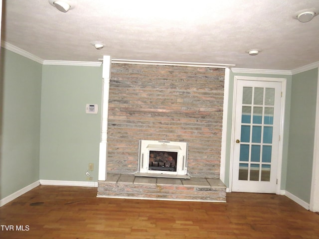 unfurnished living room featuring a fireplace with raised hearth, crown molding, baseboards, and wood finished floors