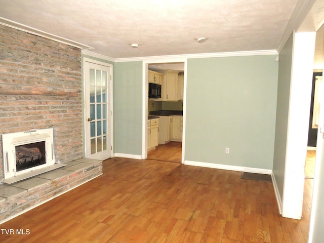 unfurnished living room with ornamental molding, a brick fireplace, baseboards, and wood finished floors