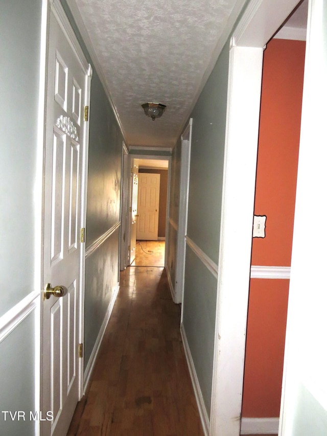 hall featuring dark wood-style flooring, a textured ceiling, and baseboards