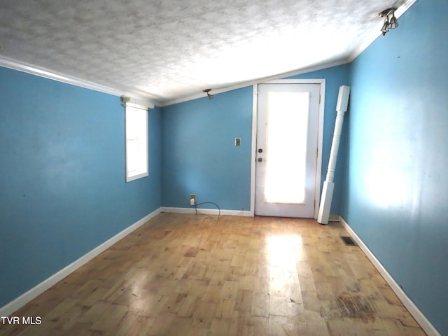 interior space with light wood-type flooring, crown molding, a textured ceiling, and baseboards