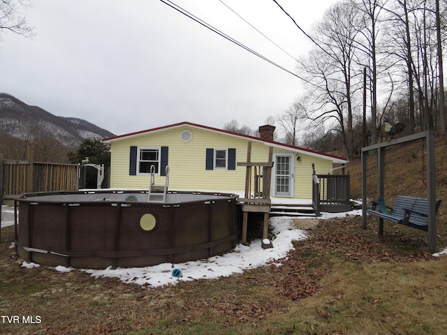 rear view of house with a deck with mountain view, a chimney, fence, and an outdoor pool