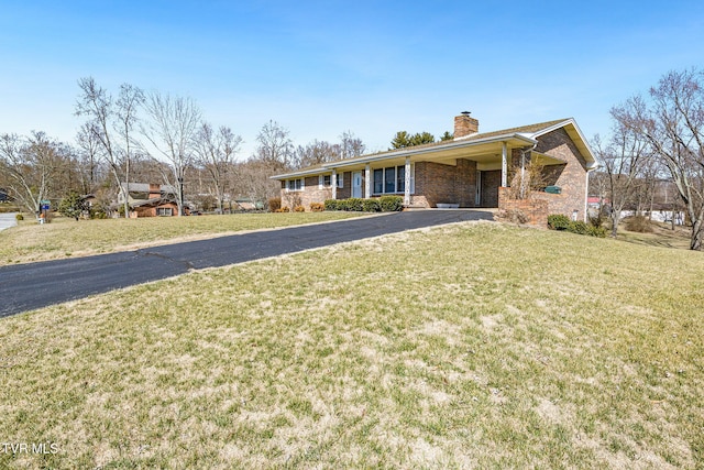 ranch-style home featuring driveway, a chimney, a front lawn, and brick siding