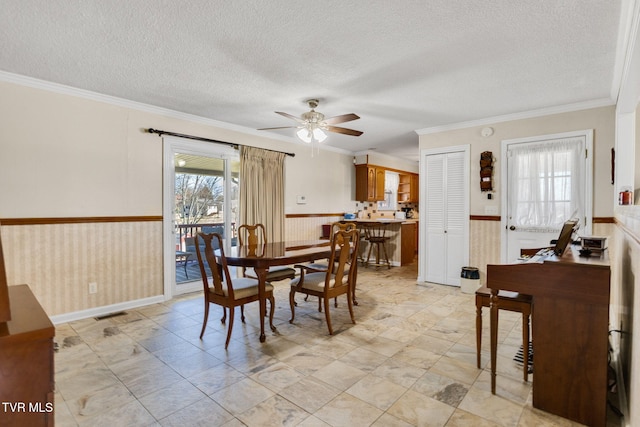 dining space featuring a wainscoted wall, crown molding, visible vents, ceiling fan, and a textured ceiling