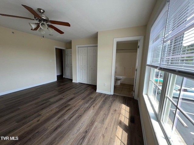 unfurnished bedroom featuring a closet, dark wood-style flooring, ensuite bath, and baseboards