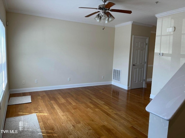 empty room with visible vents, ornamental molding, a ceiling fan, wood finished floors, and baseboards