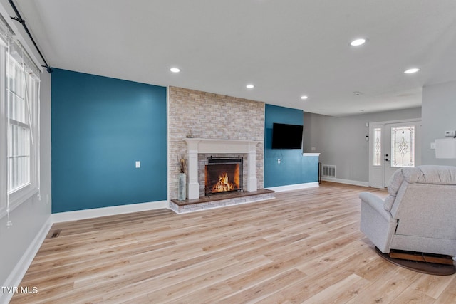 unfurnished living room featuring wood finished floors, visible vents, baseboards, recessed lighting, and a brick fireplace