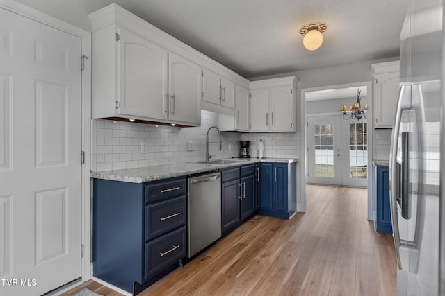 kitchen with blue cabinetry, a sink, white cabinets, light wood-style floors, and appliances with stainless steel finishes