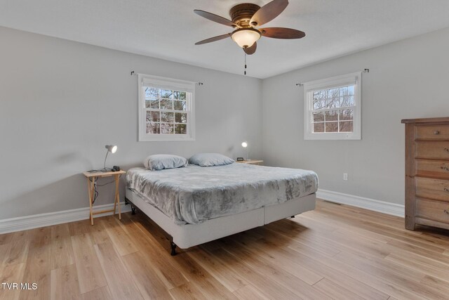 bedroom featuring baseboards, multiple windows, ceiling fan, and light wood finished floors