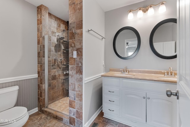 bathroom featuring toilet, a wainscoted wall, a tile shower, and a sink