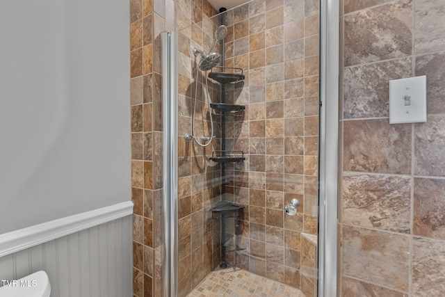 bathroom featuring a shower stall, toilet, and a wainscoted wall