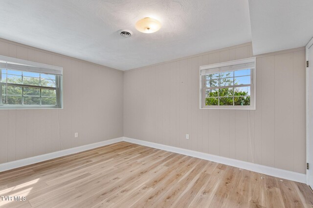 empty room featuring plenty of natural light, visible vents, and light wood-style floors