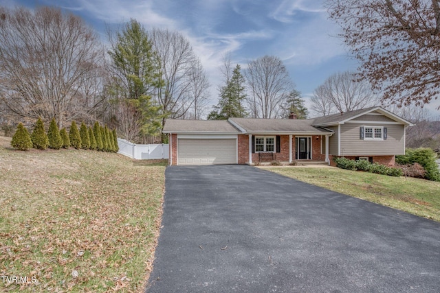 split level home featuring a garage, brick siding, aphalt driveway, and fence