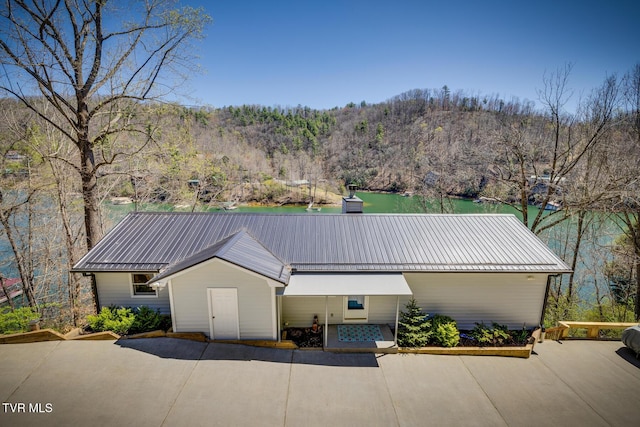 view of front facade with a forest view, a chimney, metal roof, and a standing seam roof