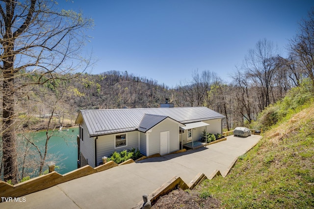 view of front of property with metal roof, a forest view, a chimney, and a water view